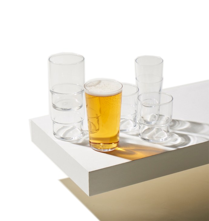 Stacking tumblers by Crane X Toyo-Sasaki Glass with one filled with beer and foam head, arranged on white surface.