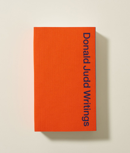 Donald Judd Writings book with orange cover and blue typography.