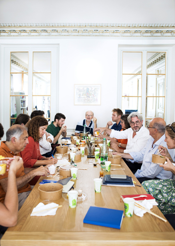 Team members at Le 1 newspaper gather around a dining table for their weekly Monday lunch meeting in Paris.