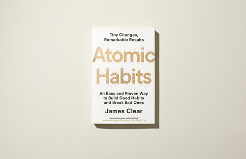 Book cover of Atomic Habits by James Clear showing title in large peach text on white background.
