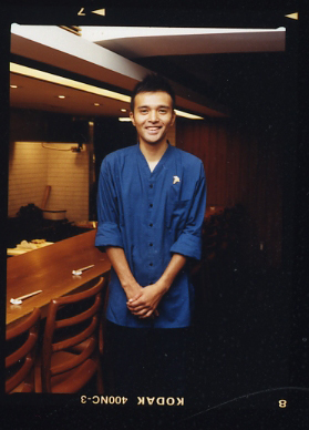 Gaku Yokokawa, manager and sommelier at izakaya Maru in Tokyo, wearing a blue shirt in the restaurant interior.