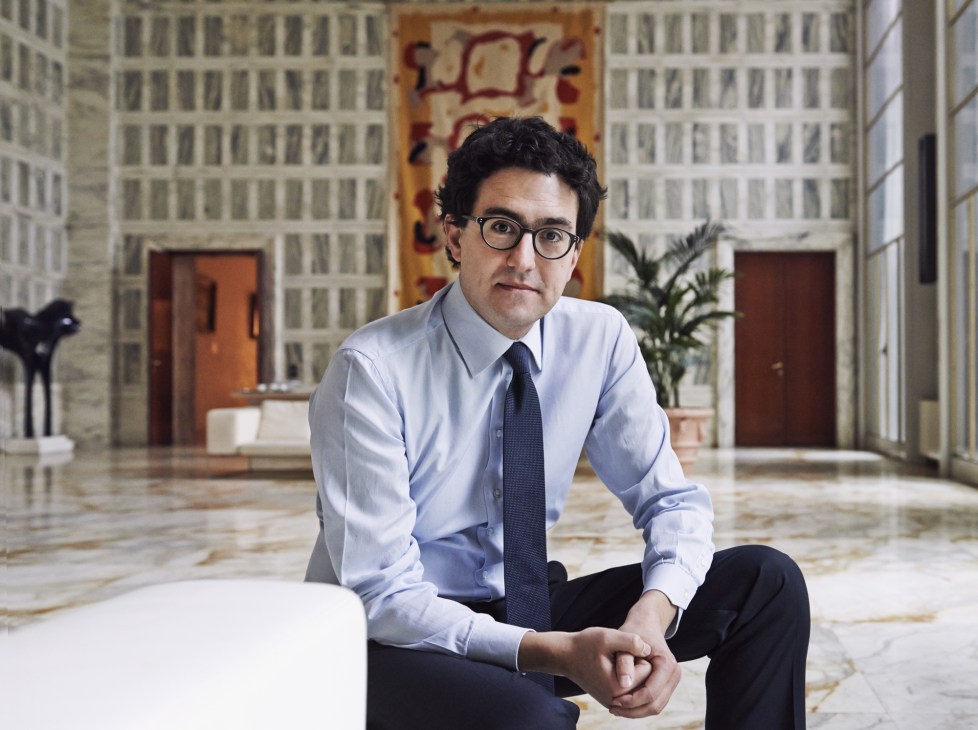 Alessandro Fusacchia, political adviser and RENA co-founder, sits in a modern architectural interior wearing glasses and business attire.