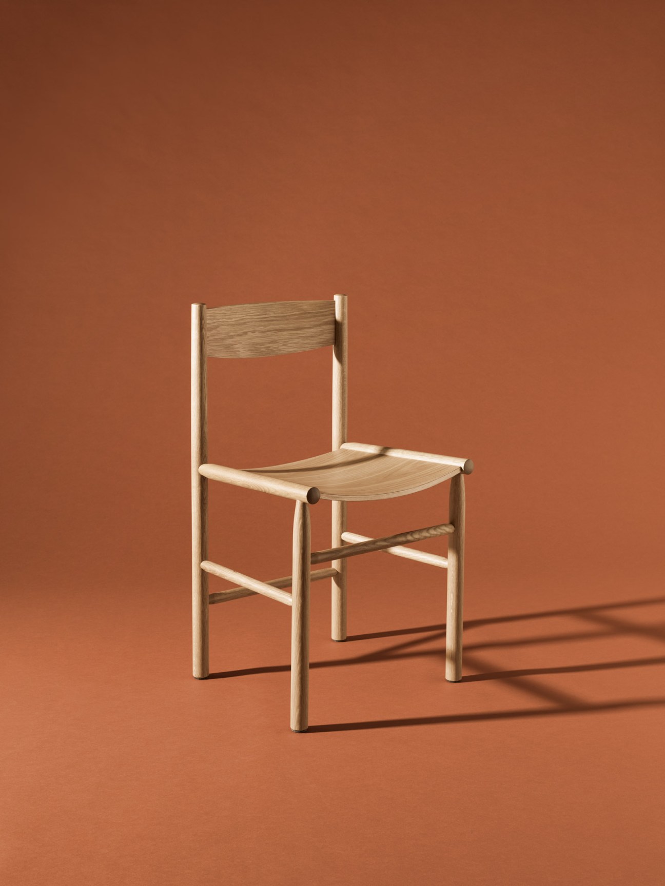 Minimalist wooden chair with curved backrest and legs against terracotta background.