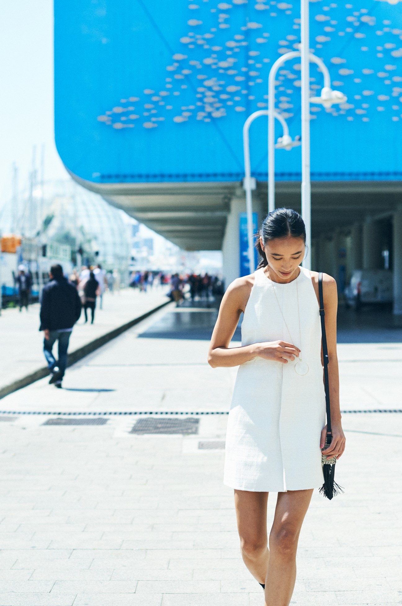 Woman in white Hermès dress with Zeus + Dione bag at a modern waterfront venue in Genoa.