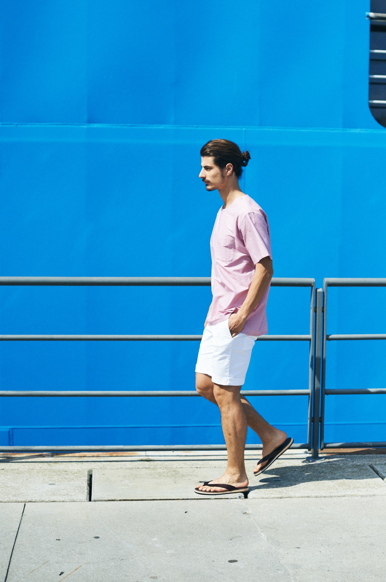 Man in pink shirt and white shorts standing on waterfront with blue wall background.