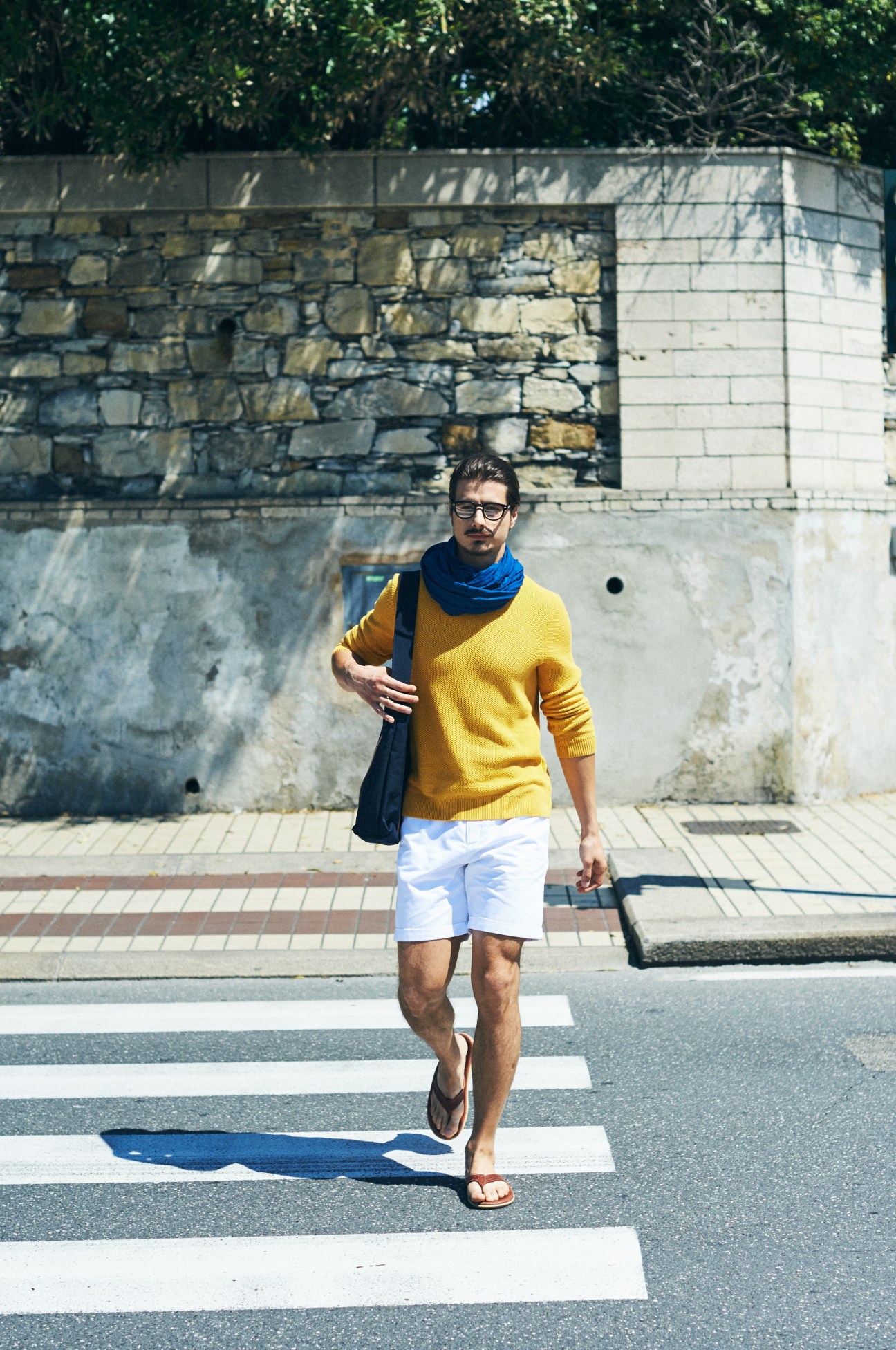 Man in yellow jumper and white shorts walking across a zebra crossing in Genoa.