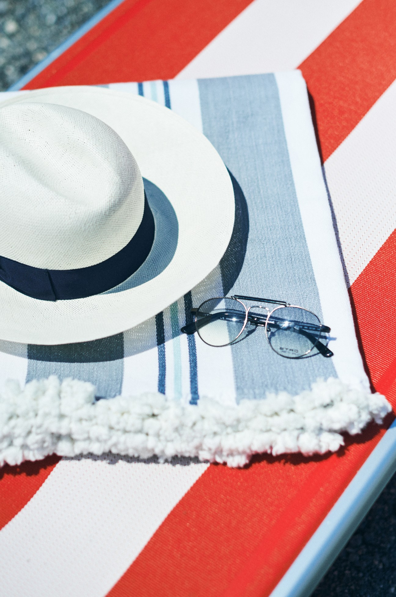 White Panama hat with dark band, sunglasses, and striped towel on red and white beach lounger.