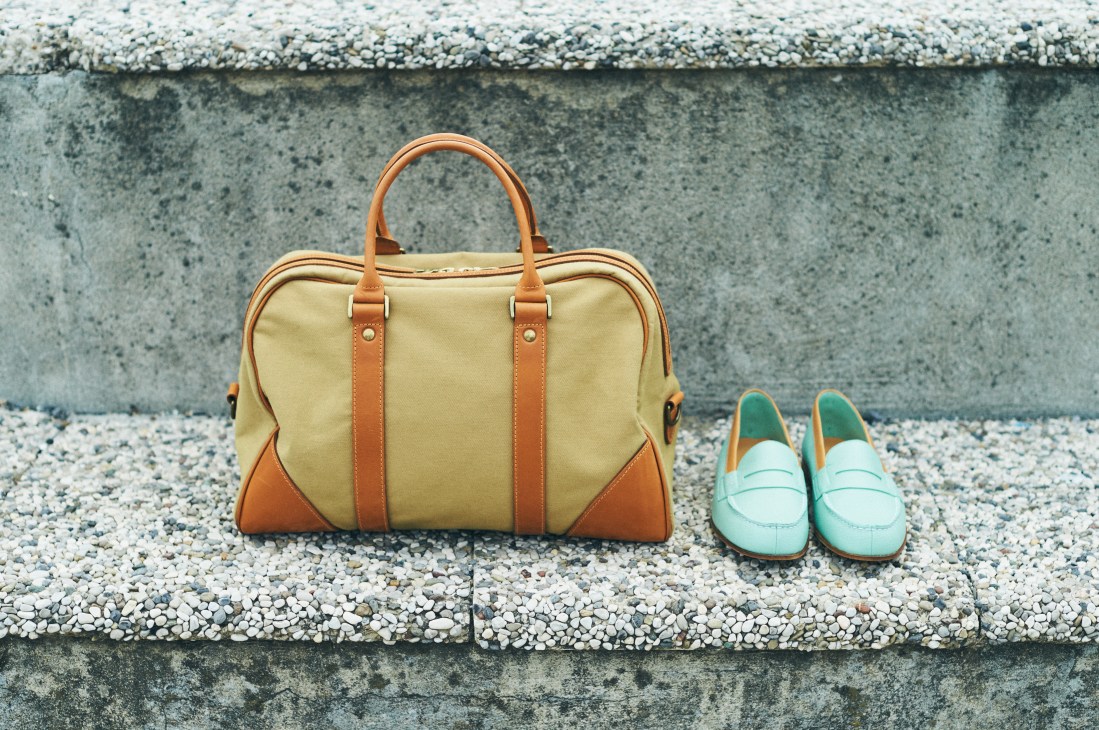 Cream canvas and tan leather handbag with JM Weston loafers in mint green on gravel.
