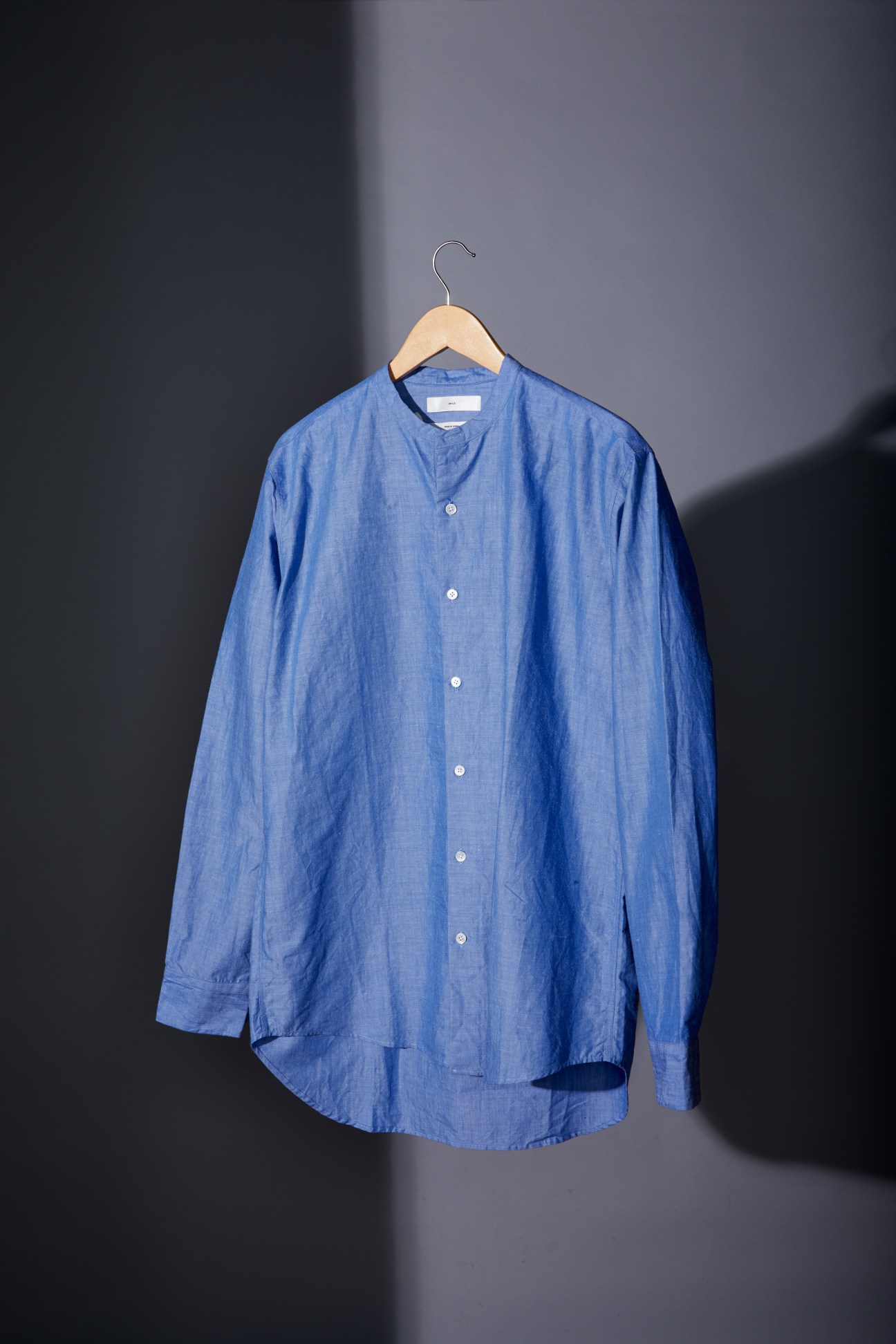 Blue linen button-up shirt on wooden hanger against gray background