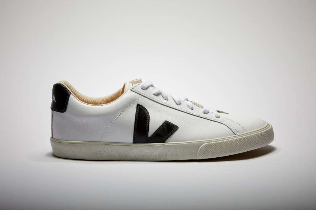 White leather sneaker with black V-shaped side stripe and cream rubber sole against gray background.