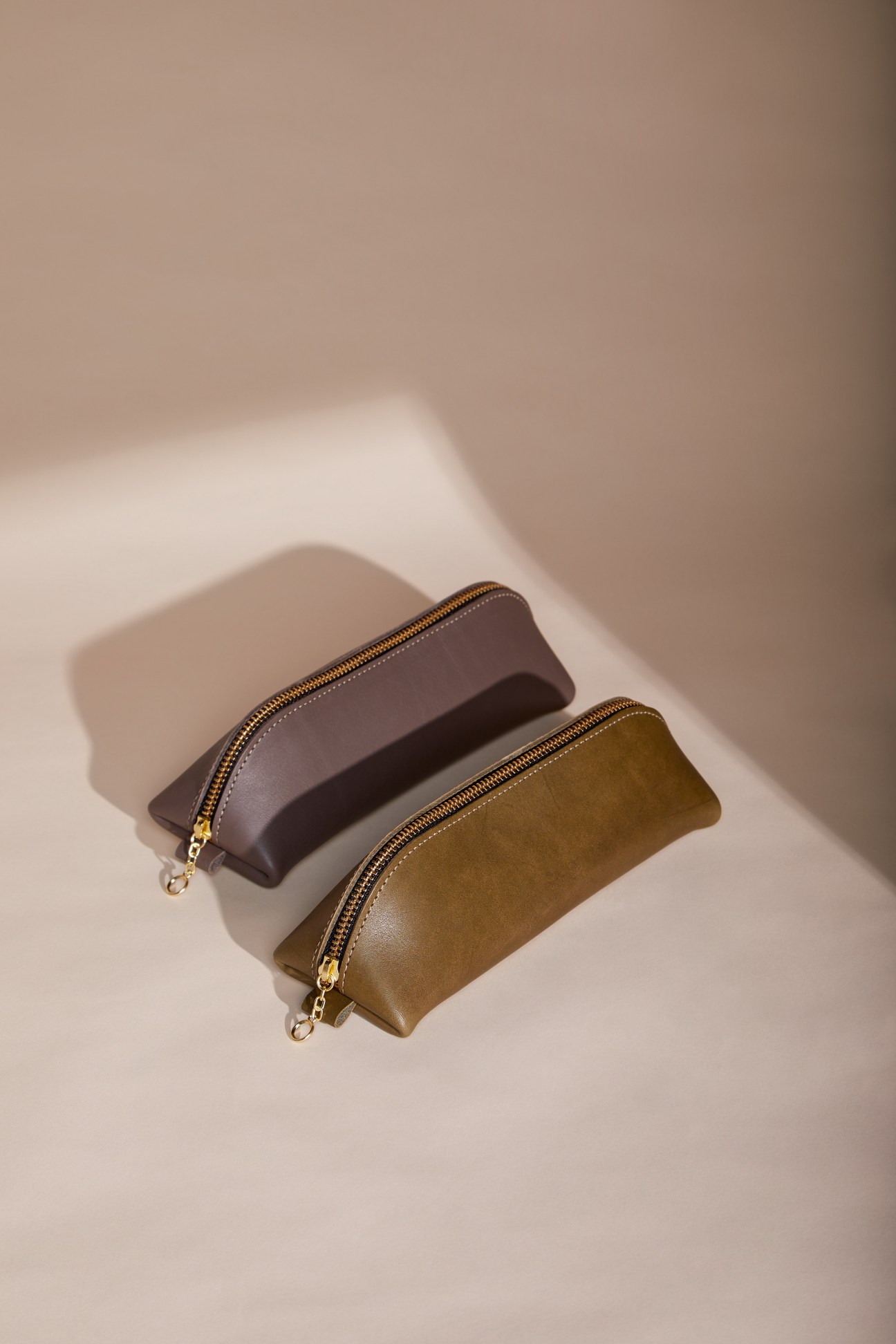 Two handcrafted leather pencil cases in brown and olive colors with gold zippers