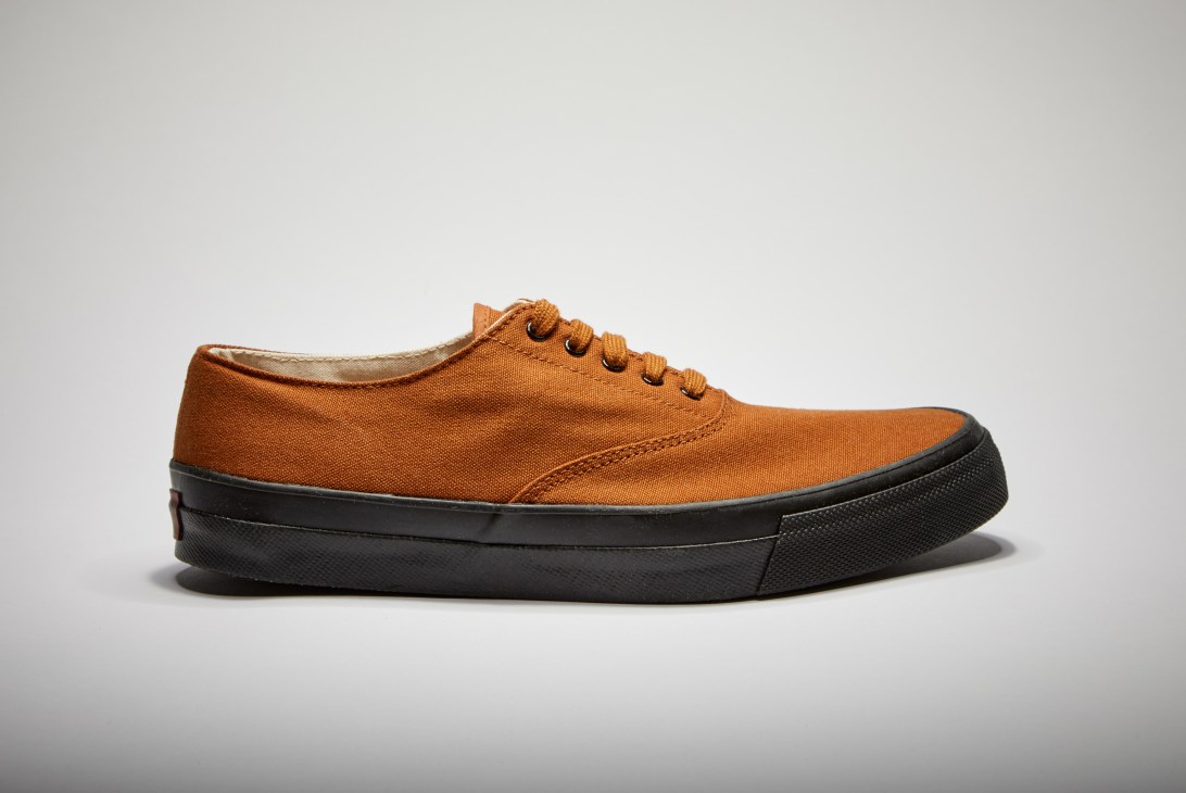 Common Projects minimalist sneaker with rust canvas upper and black sole.