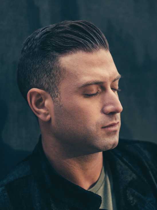 Profile portrait of Omar Sharif Jr, a man with dark hair styled back, wearing a dark jacket against a teal background.