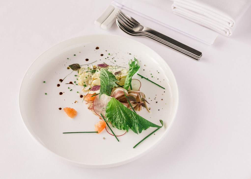 Plated Iberian pig-ear salad with cauliflower, grapefruit, greens and microgreens on white dish.