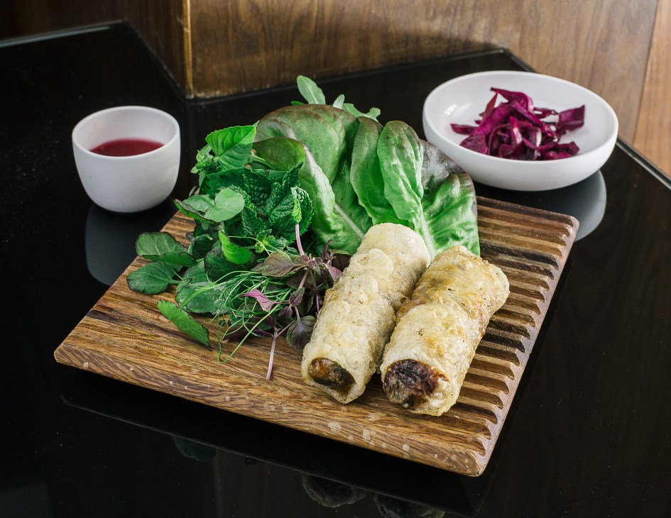Vietnamese Nem rolls plated on wooden board with fresh lettuce, dipping sauce and beetroot garnish.