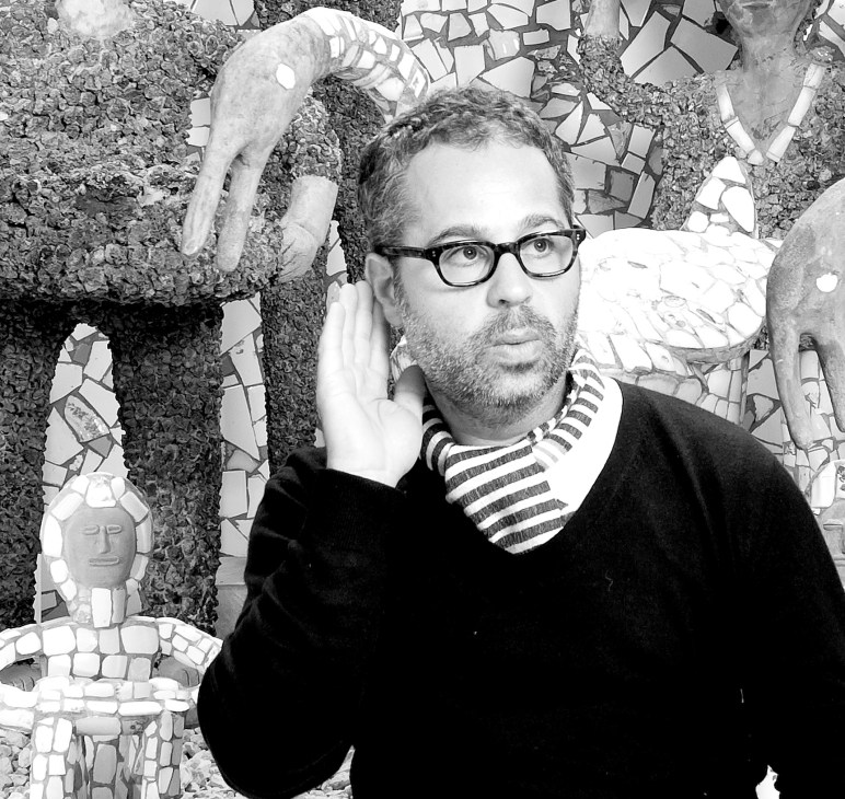 Man with glasses and beard wearing striped shirt in front of mosaic artwork