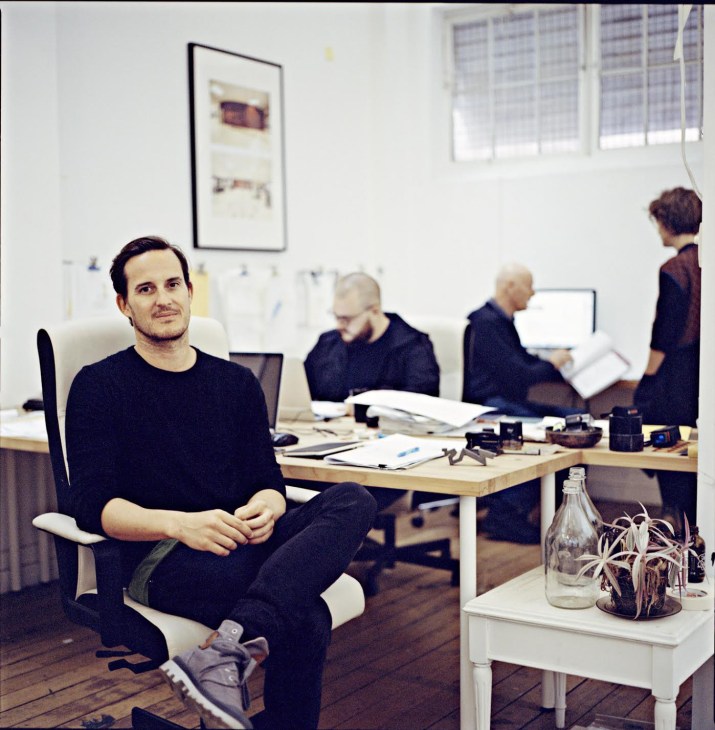 Nic Brunsdon sits at a desk in a bright Perth architecture studio with colleagues working in the background.