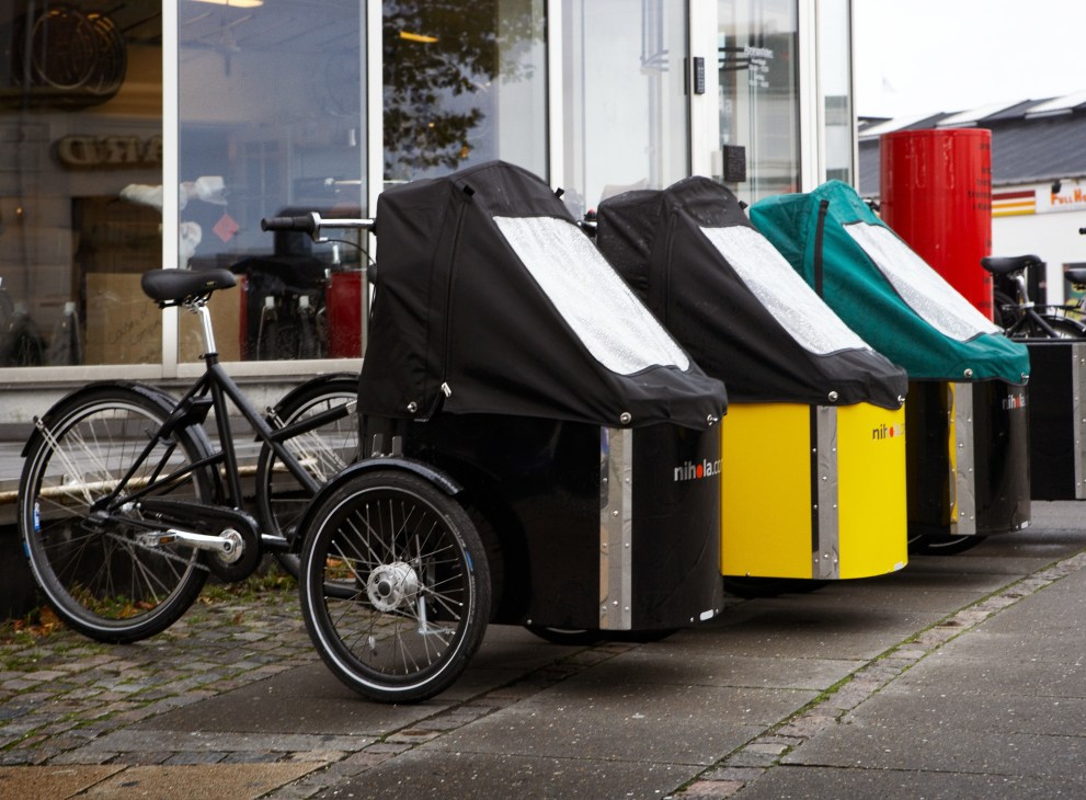 Nihola cargo bikes parked on a Copenhagen street, with colorful covered compartments in black, yellow, teal and red.