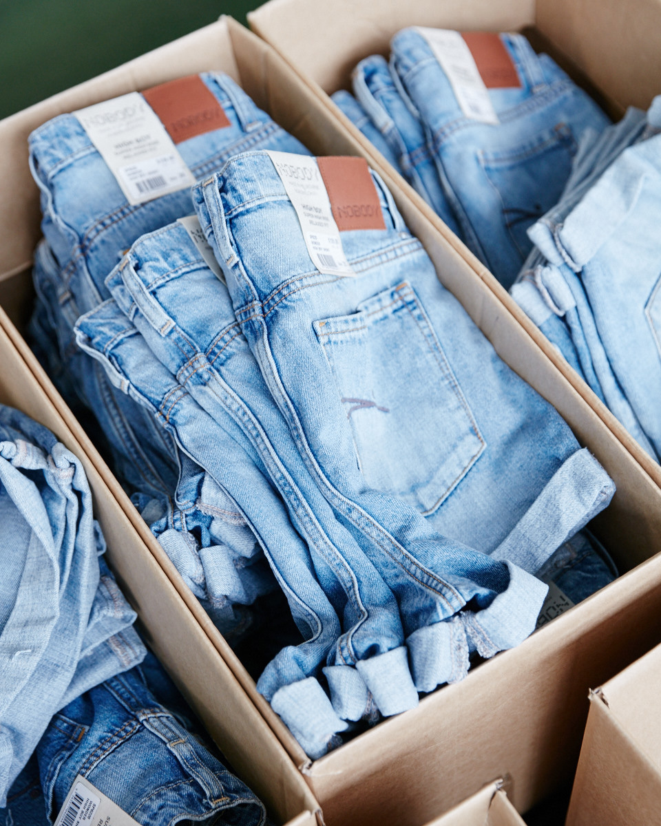 Folded denim jeans with white and rust-colored labels stacked in cardboard boxes.
