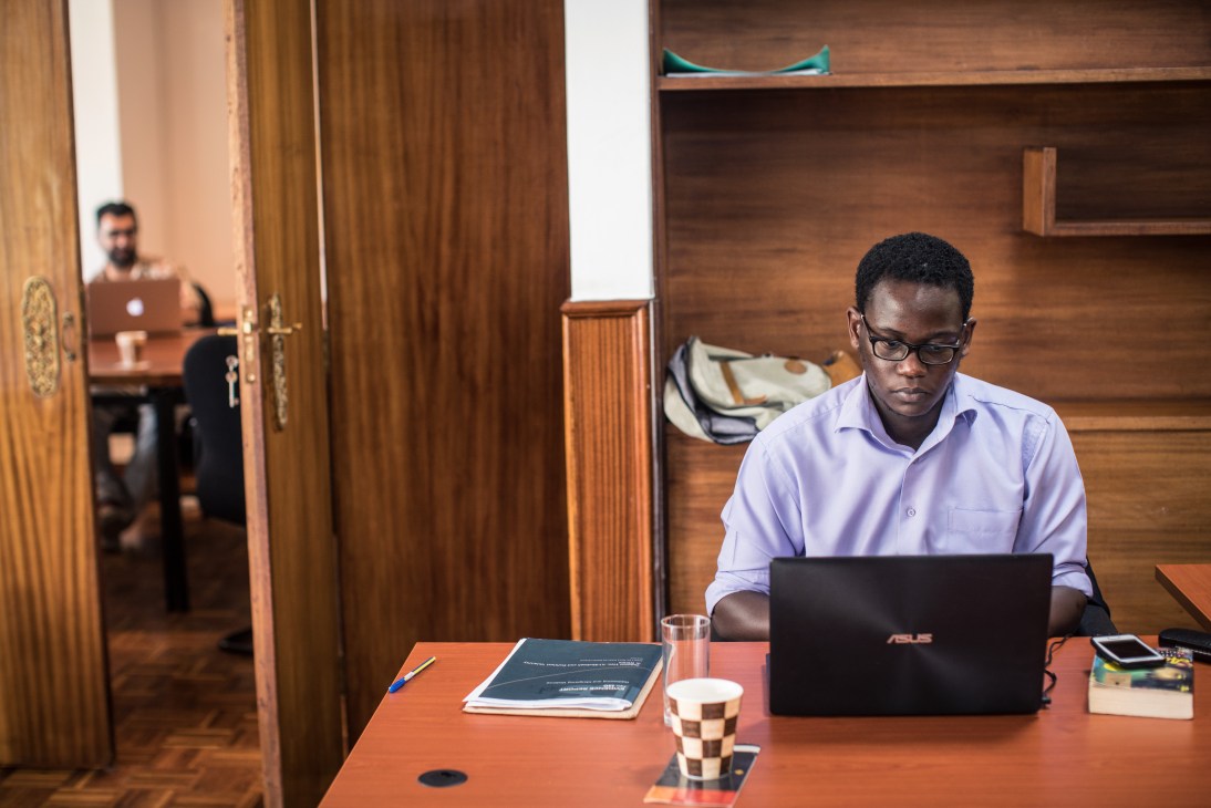 A researcher at Sahan Research in Nairobi works at a desk with a laptop in a wood-paneled office.