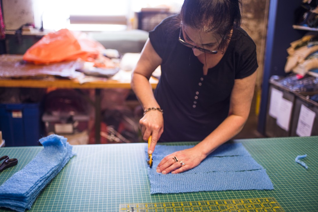 A craftsperson works on blue knitwear at a cutting table in Ohio Knitting Mills factory.