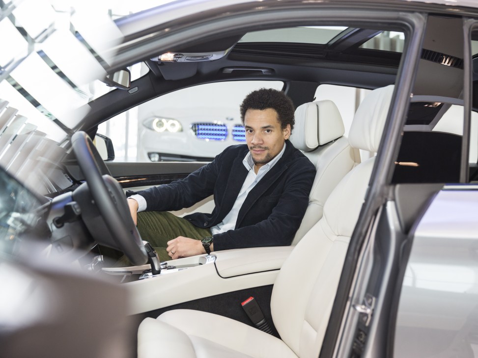 Oliver Heilmer, BMW interior designer, sits in a car's driver seat examining the dashboard and steering wheel design.