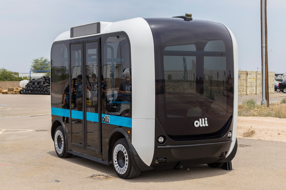 Local Motors' Olli autonomous minibus, a white and dark pod-shaped vehicle with blue accents and passengers visible through windows.