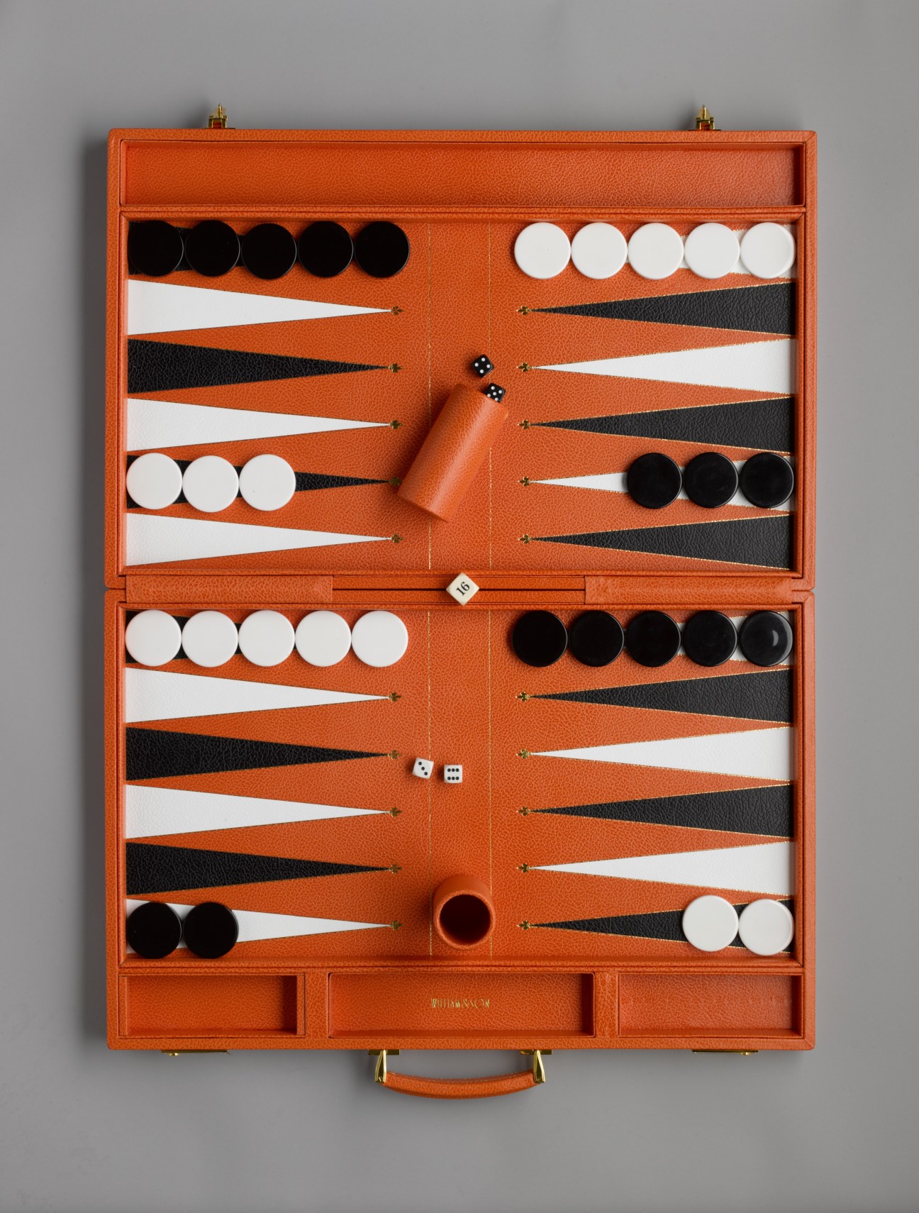 Orange leather backgammon board with black and white pieces and dice arranged on playing surface.