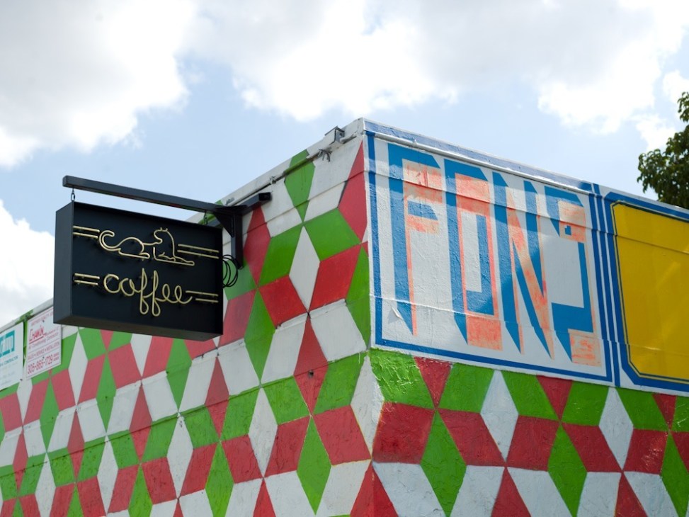 Exterior of Panther Coffee in Miami with colorful geometric mural and gold neon coffee sign.