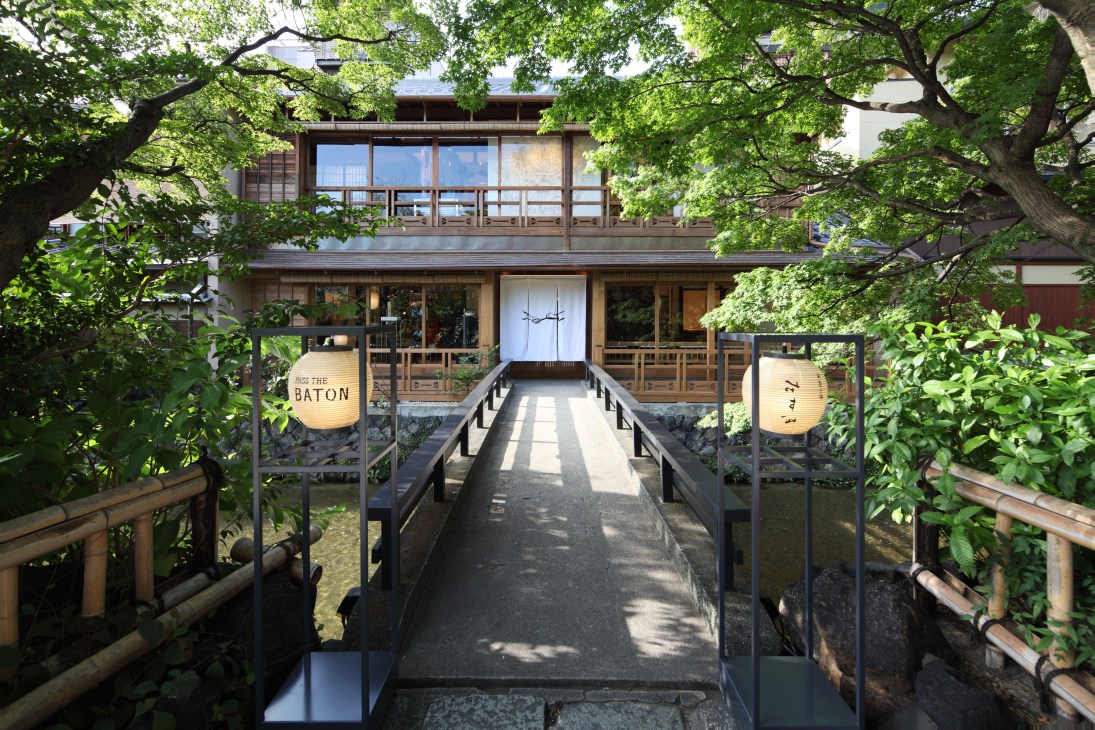 Pass the Baton shop entrance in Kyoto's Gion district, a wooden traditional townhouse with walkway and lantern signage.