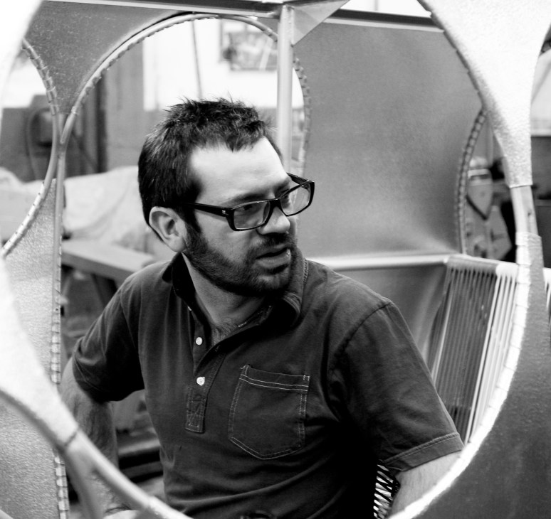 Black and white portrait of Pedro Reyes, architecture-trained artist, wearing glasses and a dark shirt.