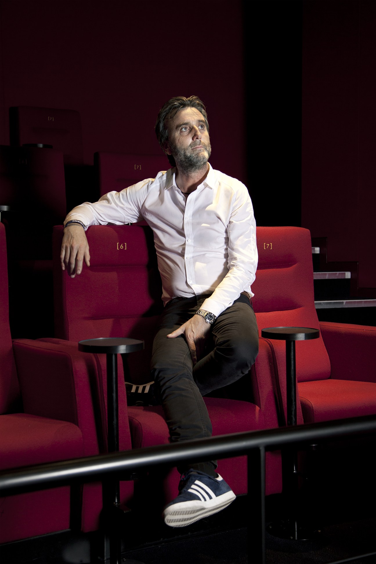 Philip Knatchbull sits in a modern cinema with burgundy seats, wearing a white shirt and dark trousers.