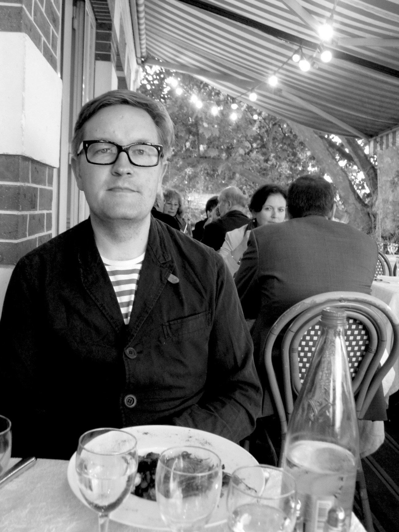 Man wearing glasses and dark jacket seated at restaurant table during meal service.