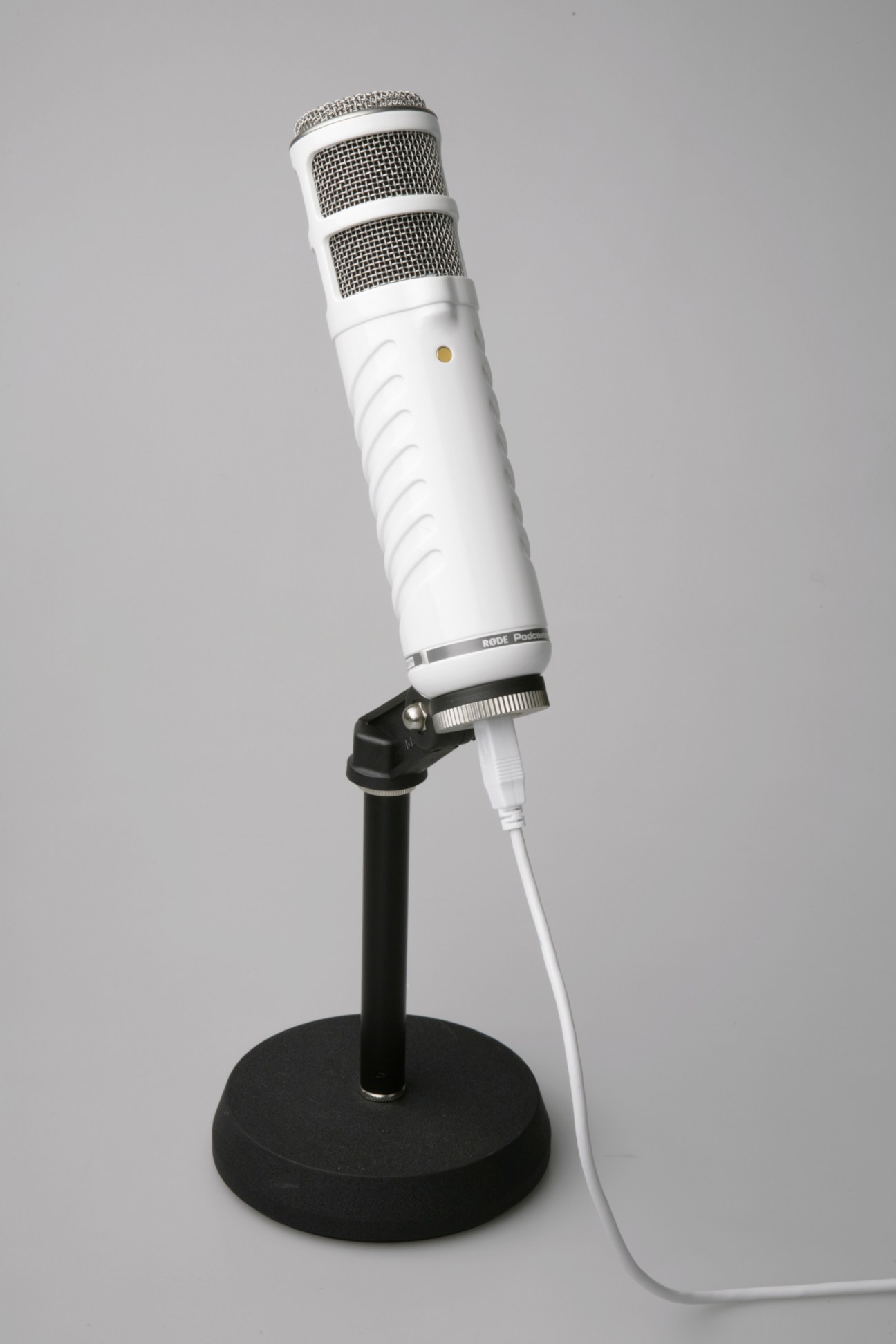 White Røde microphone with mesh grille mounted on black stand against grey background.