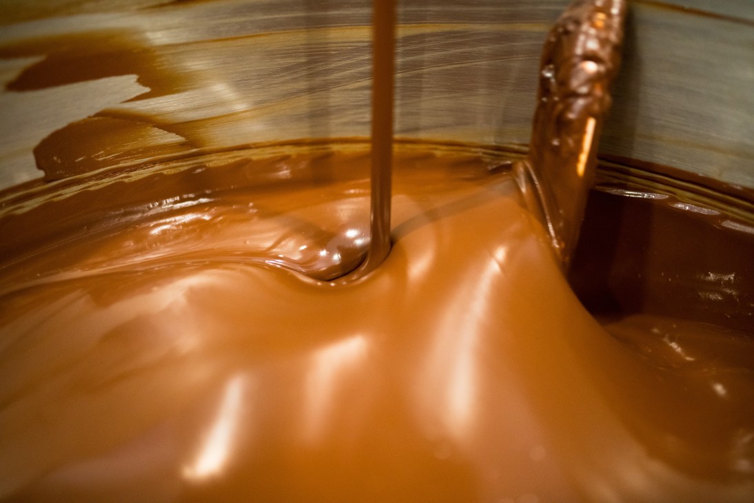 A metal spoon stirring melted chocolate in a container during the tempering process.