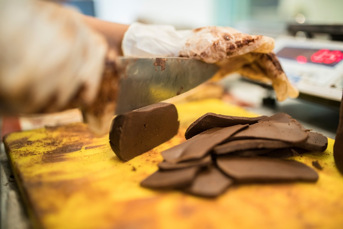 Chocolate pieces on a yellow surface with grinding equipment and cocoa powder visible.