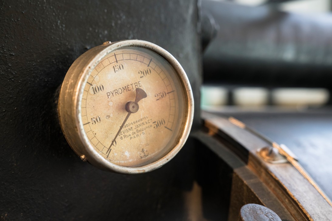 Vintage brass pyrometer gauge measuring temperature on Marou's custom-built cocoa bean deshelling machine.