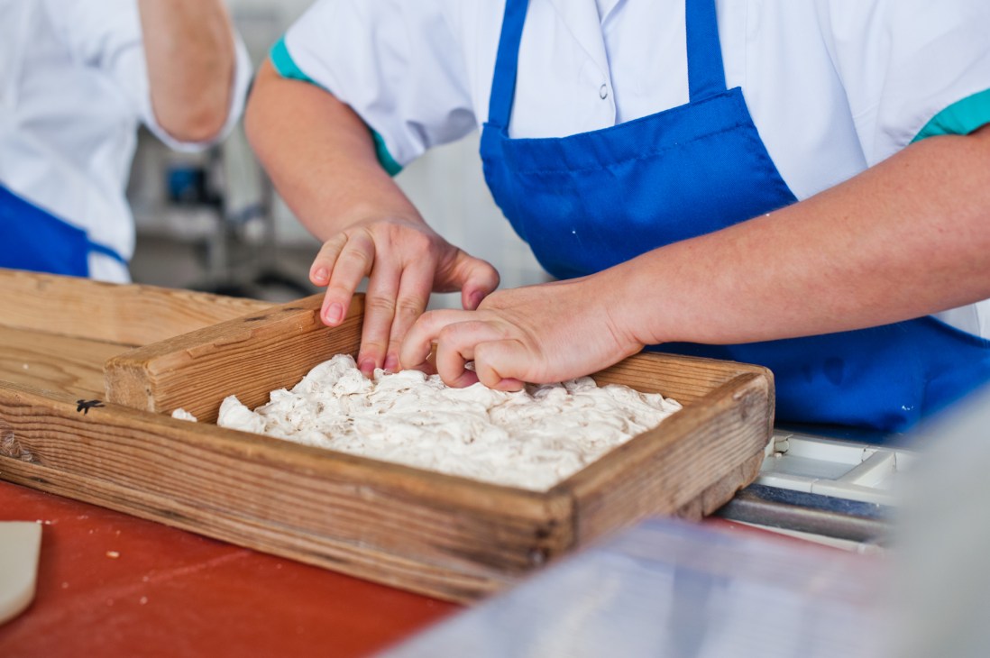 Factory worker in blue apron hand-shaping nougat mixture on a wooden moulding table.