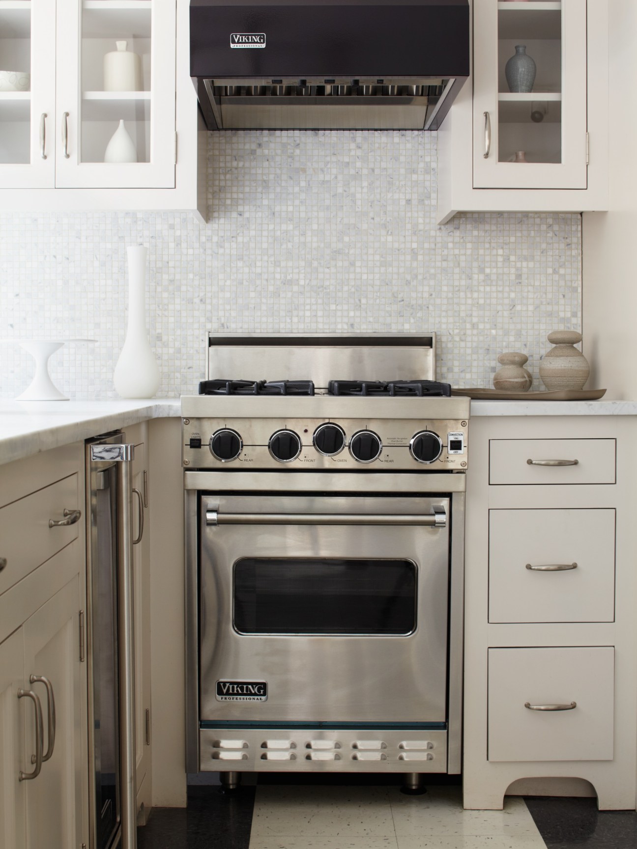 Viking Professional stainless steel range with black knobs in white kitchen cabinetry with tile backsplash.
