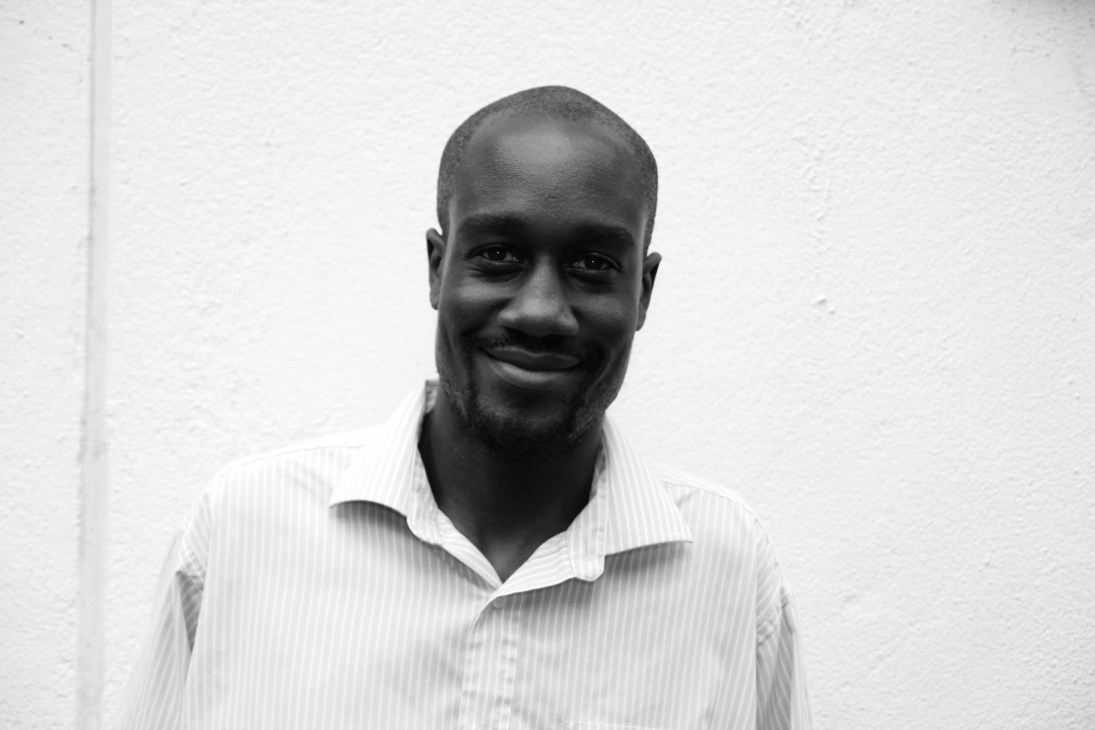 Black and white portrait photograph of a man wearing a white pinstriped shirt against a white background.