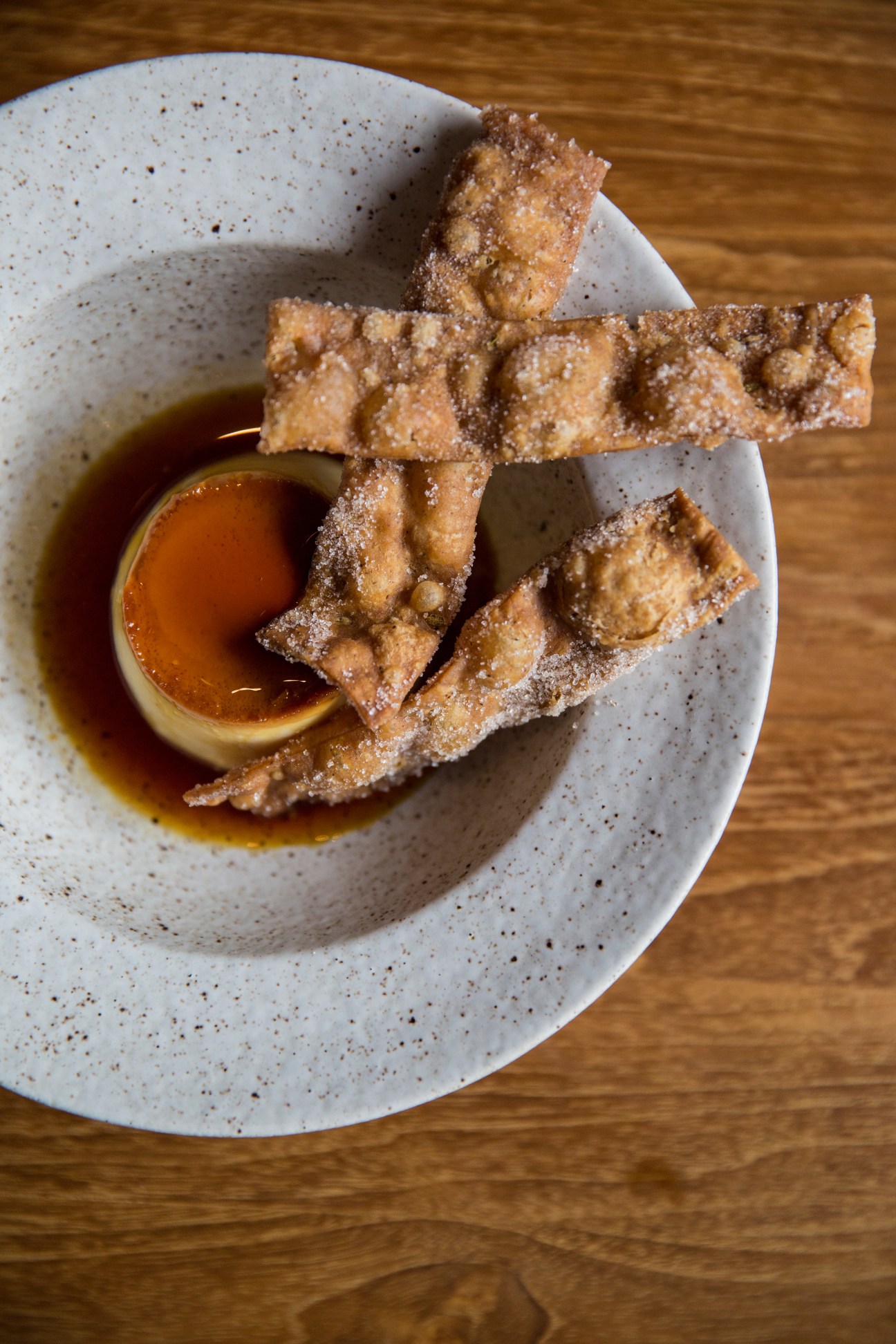 Fried churros dusted with sugar arranged on a speckled ceramic plate with a caramel dipping sauce.