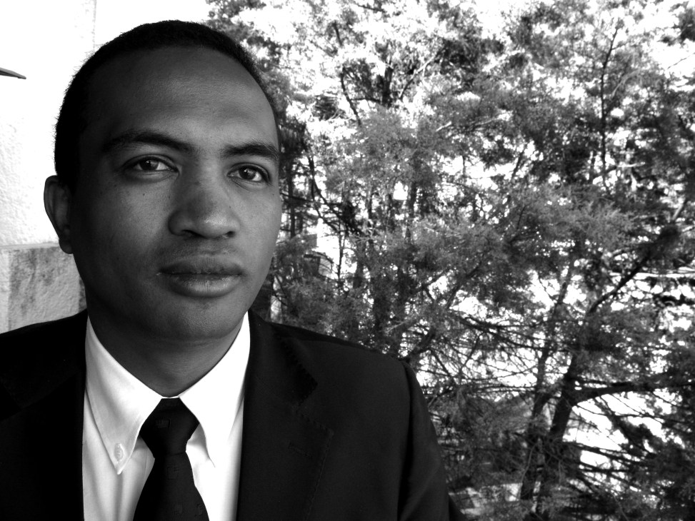 Black and white portrait of Andry Andriamanga, executive secretary of Voahary Gasy, wearing a suit and tie with foliage visible in the background.