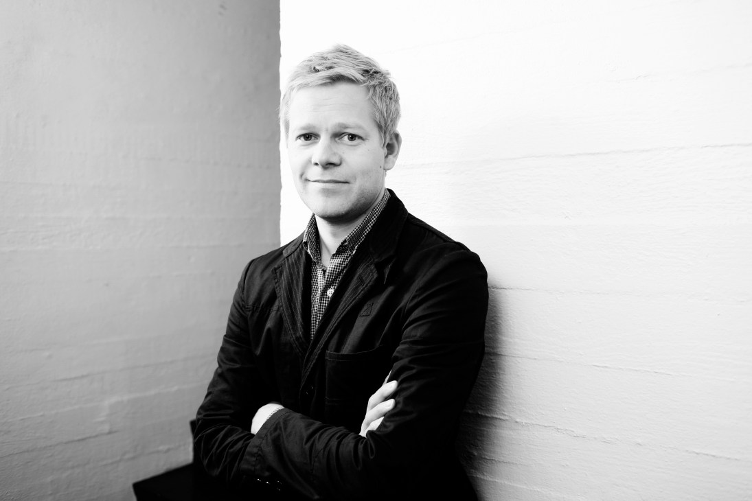 Black and white portrait of Ville Kokkonen, design director at Artek, standing against a white wall.