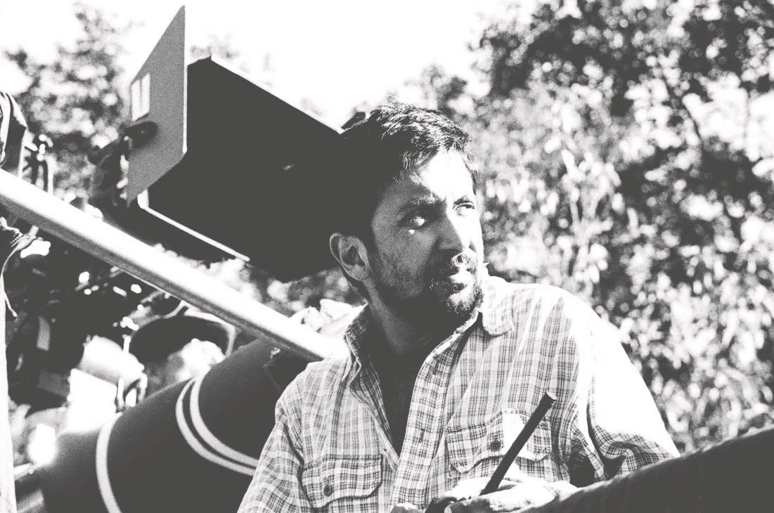 Black and white photograph of filmmaker Ashvin Kumar holding a professional camera outdoors.