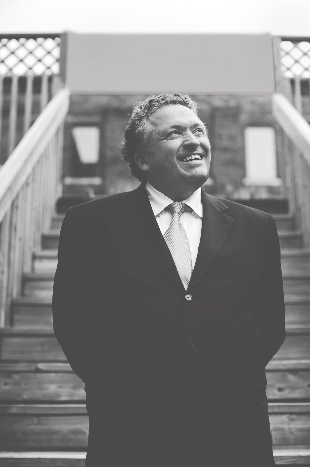 Designer Bruce Mau smiling outdoors in a dark suit and striped tie.