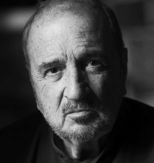 Black and white portrait photograph of Jean-Claude Carrière, a bearded older man with receding hair looking directly at the camera.