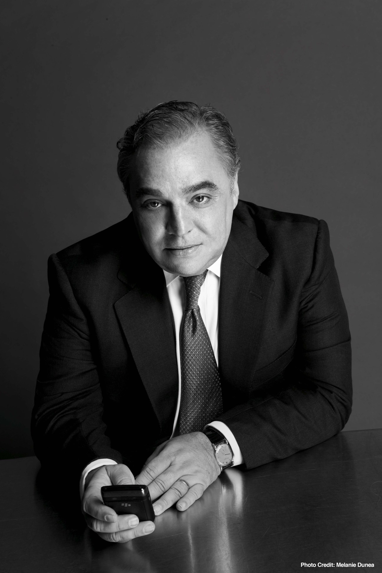 Black and white portrait of Lee Schrager in business suit holding a mobile device