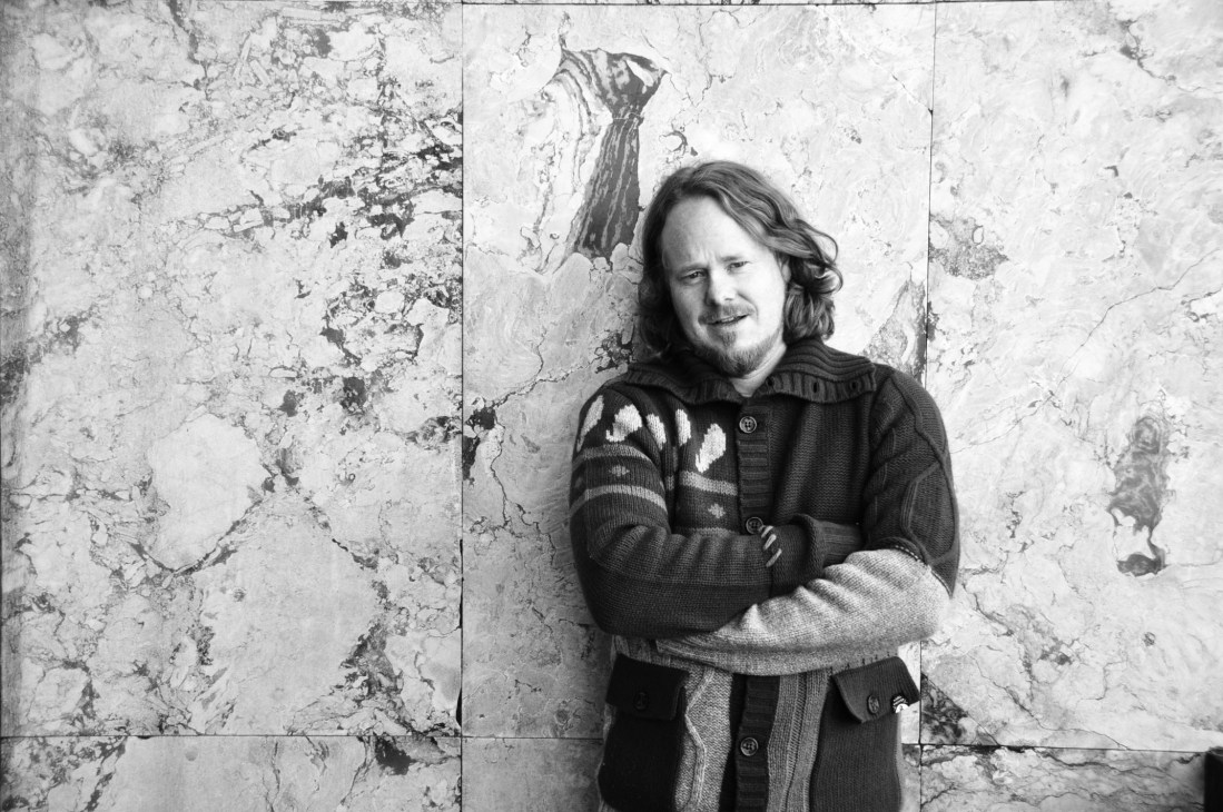 Portrait of Marius Brandl, interior designer and entrepreneur, standing against a weathered concrete wall.