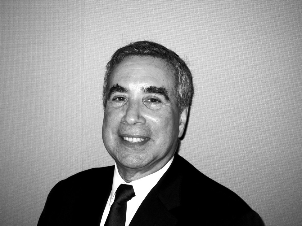 Black and white portrait photograph of Philip Aarons, a man in a dark suit and tie smiling at the camera.