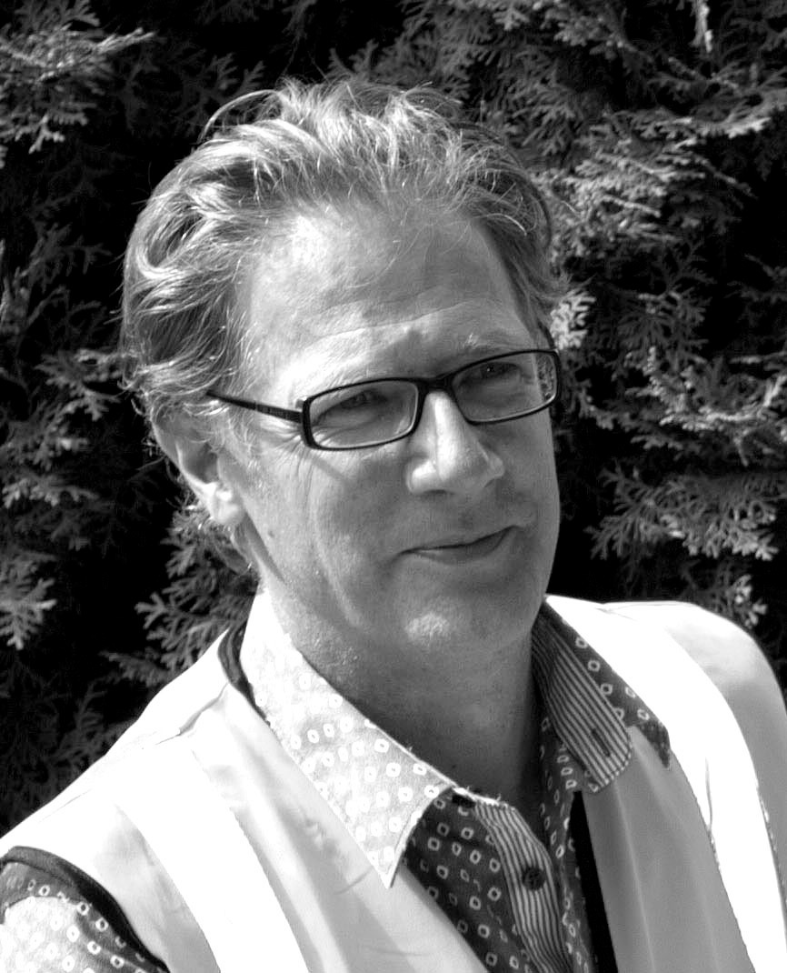 Black and white portrait of Roger Sutton, CEO of CERA, wearing glasses and a white jacket with patterned shirt.